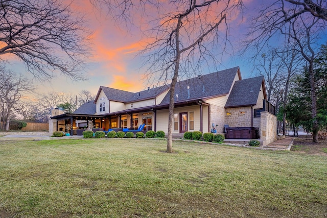 back house at dusk with a hot tub, a patio area, and a lawn