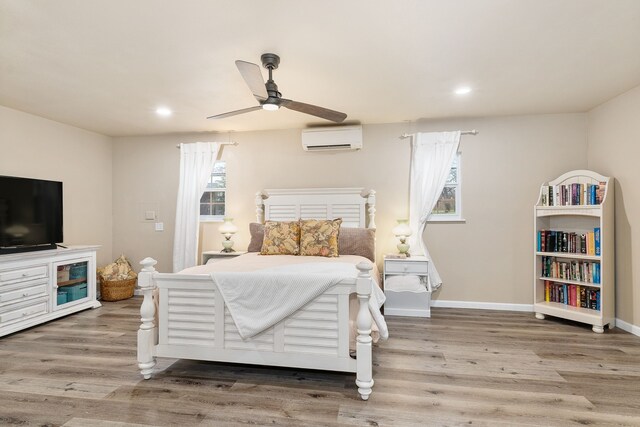 bedroom with an AC wall unit, light hardwood / wood-style flooring, a barn door, and ceiling fan