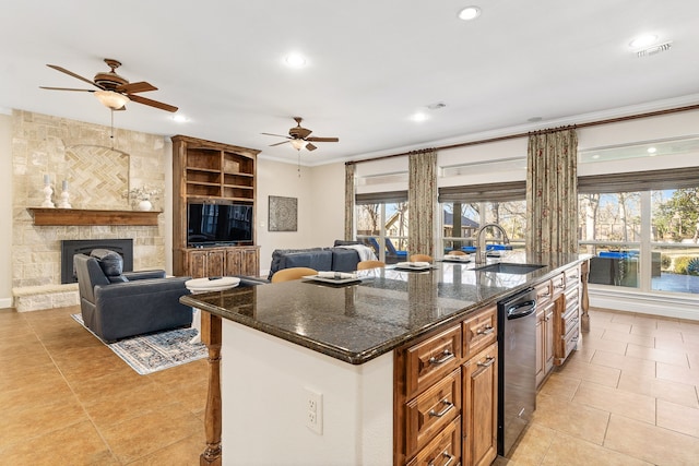 kitchen featuring an island with sink, sink, dark stone countertops, and a fireplace