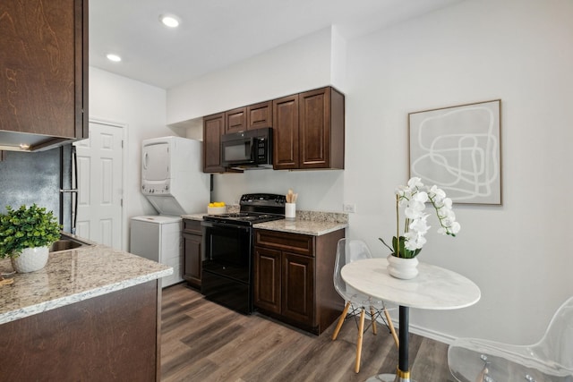 kitchen featuring stacked washer / dryer, dark brown cabinetry, black appliances, light stone countertops, and dark wood-type flooring