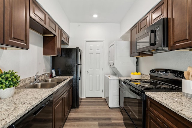 kitchen featuring dark brown cabinetry, sink, dark hardwood / wood-style floors, stacked washer / dryer, and black appliances