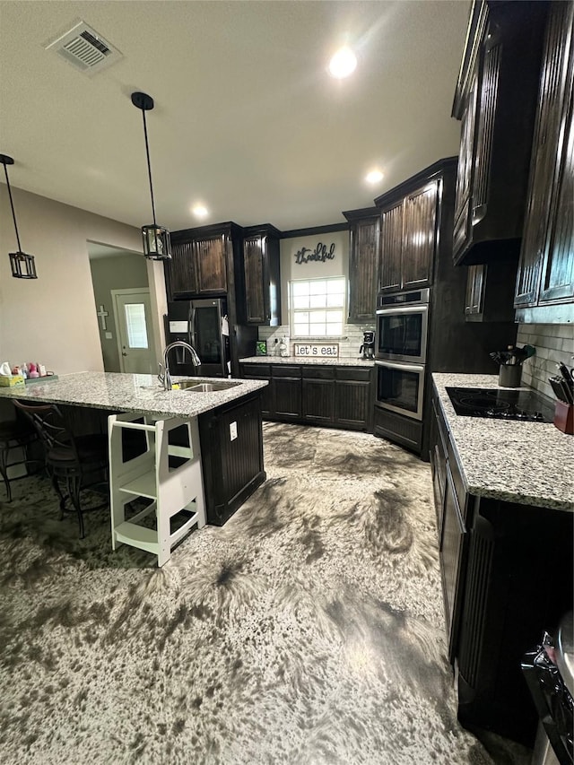 kitchen featuring hanging light fixtures, backsplash, dark brown cabinets, a center island with sink, and black electric cooktop