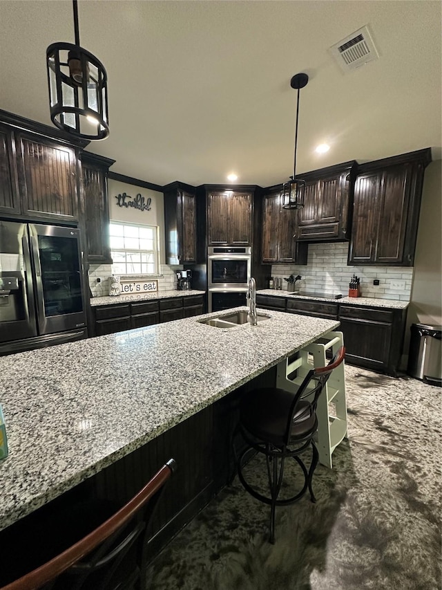 kitchen with appliances with stainless steel finishes, sink, a kitchen bar, hanging light fixtures, and dark brown cabinetry