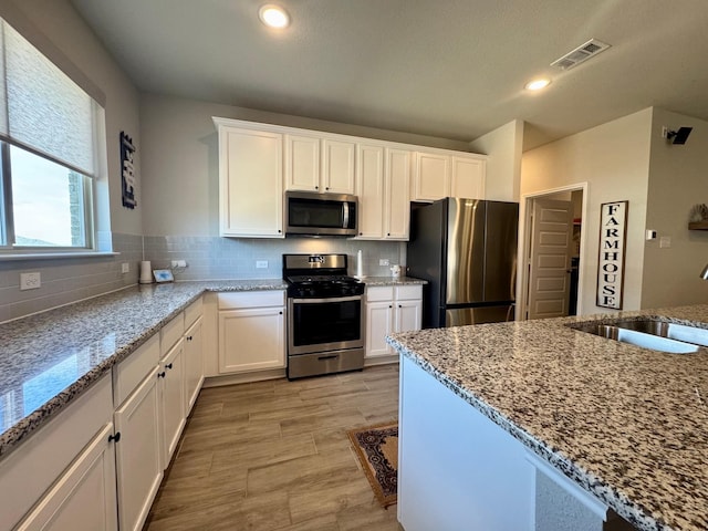 kitchen featuring sink, appliances with stainless steel finishes, white cabinetry, light stone countertops, and decorative backsplash