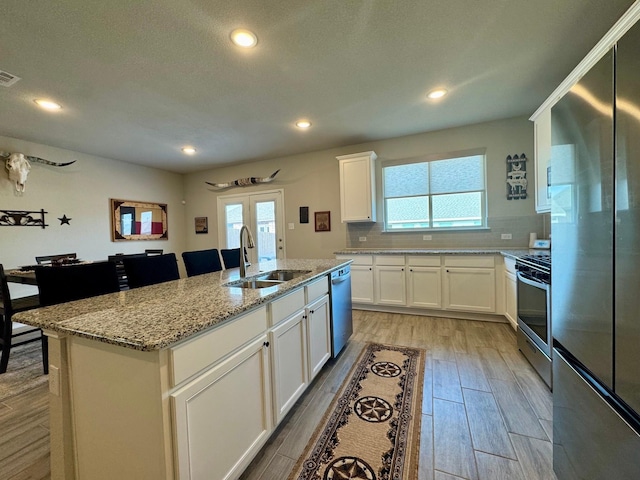 kitchen featuring sink, white cabinets, a kitchen island with sink, stainless steel appliances, and light stone countertops