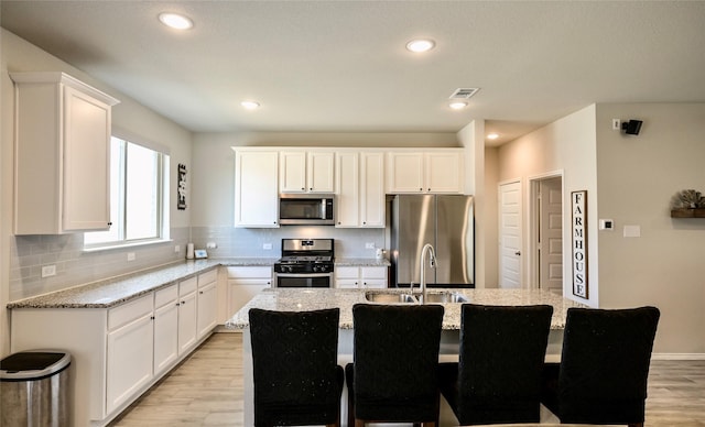 kitchen featuring light stone countertops, appliances with stainless steel finishes, sink, and a center island with sink