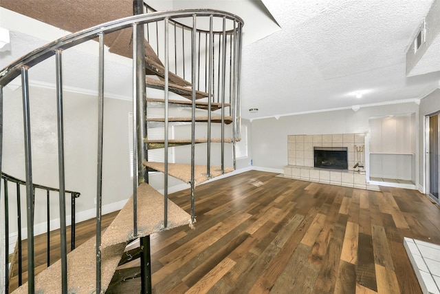 unfurnished living room with crown molding, a tiled fireplace, hardwood / wood-style floors, and a textured ceiling