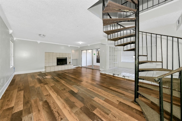 unfurnished living room featuring crown molding, a tiled fireplace, hardwood / wood-style floors, and a textured ceiling