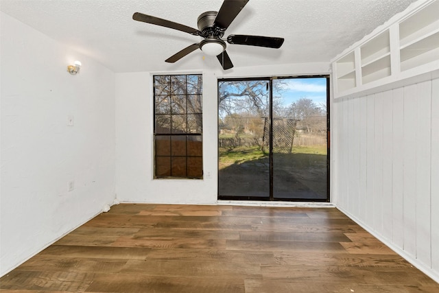 empty room with ceiling fan, dark hardwood / wood-style floors, a textured ceiling, and wood walls