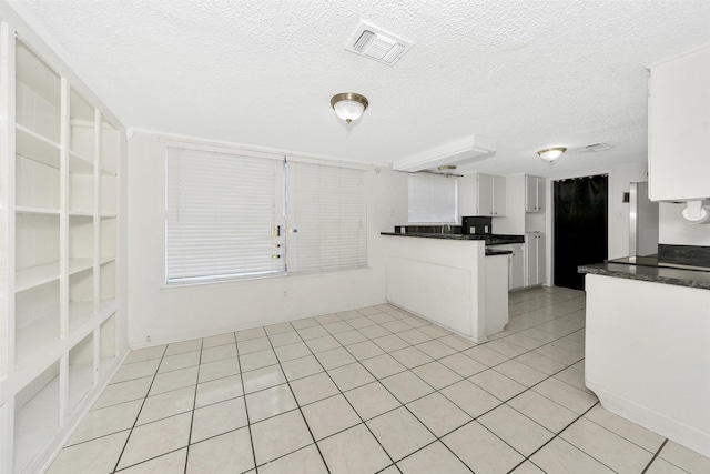 kitchen with light tile patterned floors, stainless steel fridge, a textured ceiling, white cabinets, and kitchen peninsula