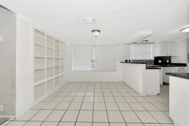 kitchen with tasteful backsplash, white cabinets, light tile patterned floors, a textured ceiling, and built in shelves