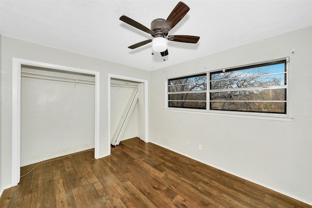 unfurnished bedroom with two closets, a textured ceiling, dark hardwood / wood-style floors, and ceiling fan