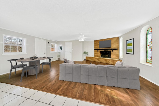 living room featuring ceiling fan, a brick fireplace, light tile patterned floors, and a textured ceiling