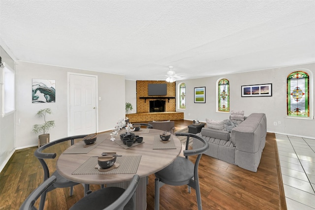 dining room with ceiling fan, dark hardwood / wood-style floors, a textured ceiling, and a brick fireplace