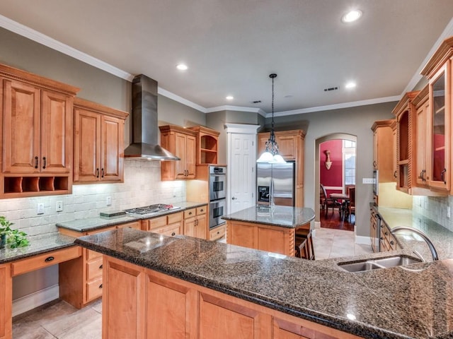 kitchen with wall chimney exhaust hood, sink, decorative light fixtures, appliances with stainless steel finishes, and a kitchen island