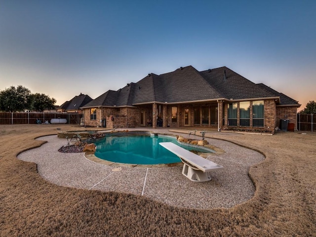 pool at dusk featuring a patio area and a diving board