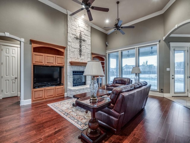 living room featuring crown molding, ceiling fan, a stone fireplace, and dark hardwood / wood-style flooring