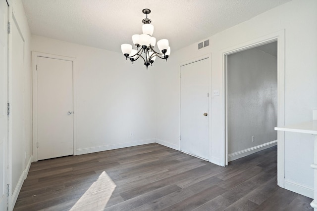 unfurnished dining area featuring dark wood-style floors, a textured ceiling, visible vents, and a notable chandelier