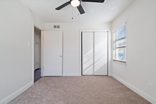 unfurnished bedroom featuring ceiling fan, a closet, light carpet, and a textured ceiling