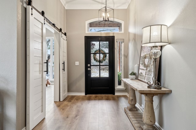 entryway featuring a notable chandelier, light hardwood / wood-style flooring, ornamental molding, and a barn door