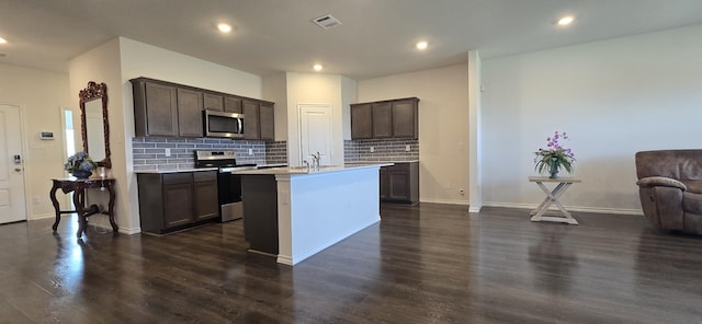 kitchen featuring dark wood-type flooring, dark brown cabinets, stainless steel appliances, tasteful backsplash, and a center island with sink