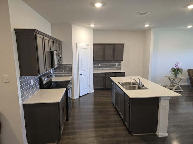 kitchen featuring sink, dark wood-type flooring, backsplash, stainless steel appliances, and a center island with sink