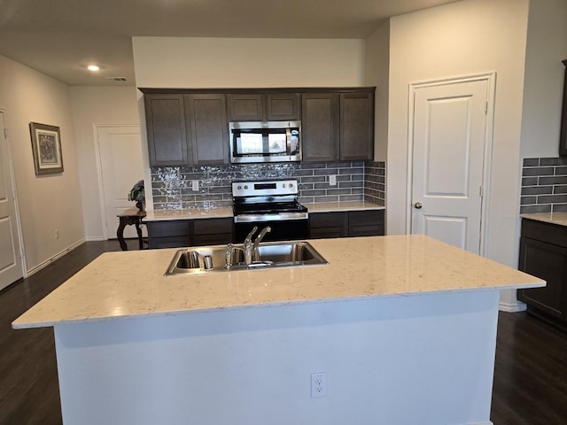 kitchen with sink, a kitchen island with sink, stainless steel appliances, tasteful backsplash, and dark brown cabinetry