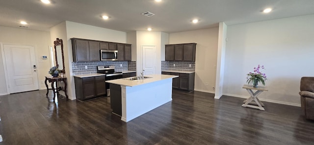 kitchen with appliances with stainless steel finishes, sink, backsplash, dark hardwood / wood-style flooring, and a center island with sink