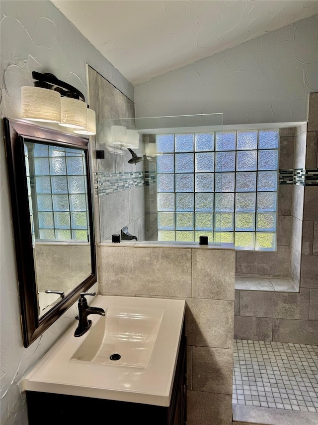 bathroom with tiled shower, vanity, and vaulted ceiling