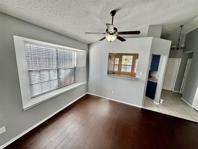 unfurnished living room with lofted ceiling, ceiling fan with notable chandelier, a textured ceiling, and light wood-type flooring