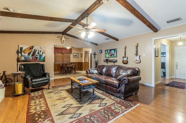 living room with lofted ceiling with beams, wood-type flooring, ceiling fan, and a textured ceiling