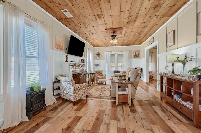 living room featuring a fireplace, a wood stove, light hardwood / wood-style floors, crown molding, and wooden ceiling