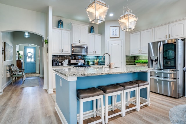 kitchen with sink, appliances with stainless steel finishes, light stone counters, white cabinets, and a center island with sink