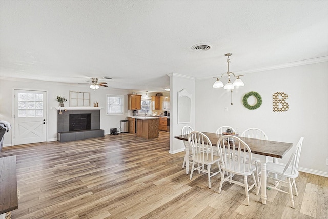 dining area with crown molding, a textured ceiling, light wood-type flooring, a tile fireplace, and ceiling fan with notable chandelier