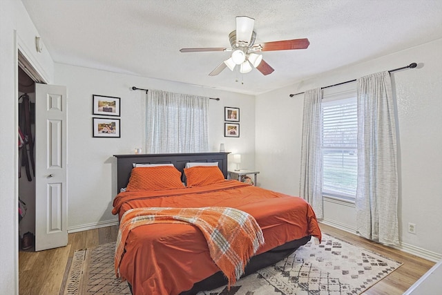 bedroom with multiple windows, a textured ceiling, ceiling fan, and light wood-type flooring