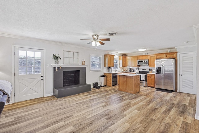 kitchen with a center island, light hardwood / wood-style floors, stainless steel appliances, crown molding, and a textured ceiling