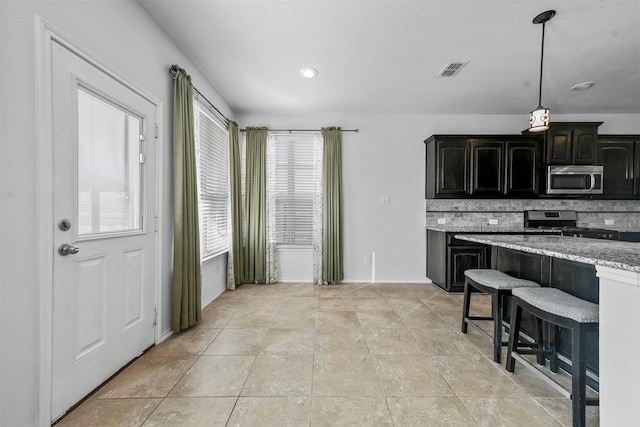 kitchen with appliances with stainless steel finishes, a breakfast bar area, backsplash, light tile patterned floors, and light stone countertops