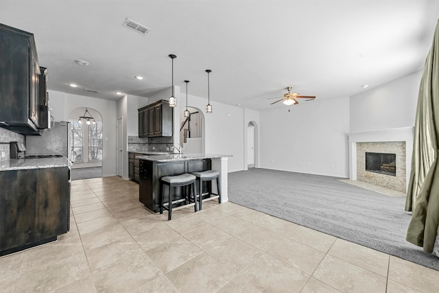 kitchen with decorative light fixtures, decorative backsplash, light colored carpet, light stone counters, and dark brown cabinetry