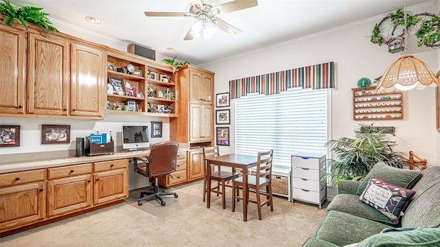 carpeted home office featuring crown molding, ceiling fan, and built in desk