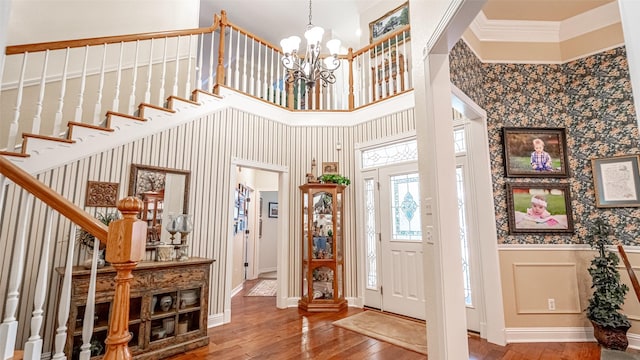 entryway with crown molding, a towering ceiling, hardwood / wood-style floors, and a chandelier