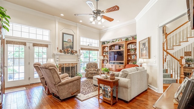 living room featuring crown molding, ceiling fan, a stone fireplace, and light hardwood / wood-style flooring