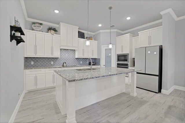 kitchen featuring an island with sink, white cabinets, crown molding, and decorative light fixtures