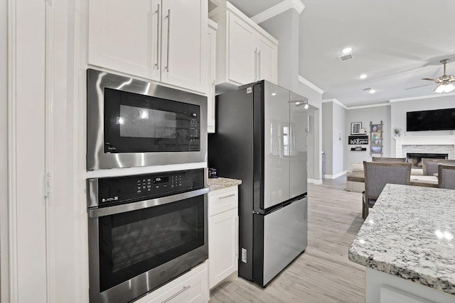 kitchen with white cabinetry, light stone counters, a stone fireplace, and appliances with stainless steel finishes