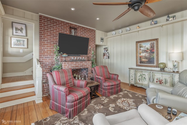 living room with ceiling fan, ornamental molding, a fireplace, and light wood-type flooring