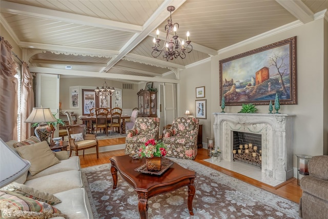 living room with beam ceiling, wood-type flooring, a chandelier, ornamental molding, and a fireplace