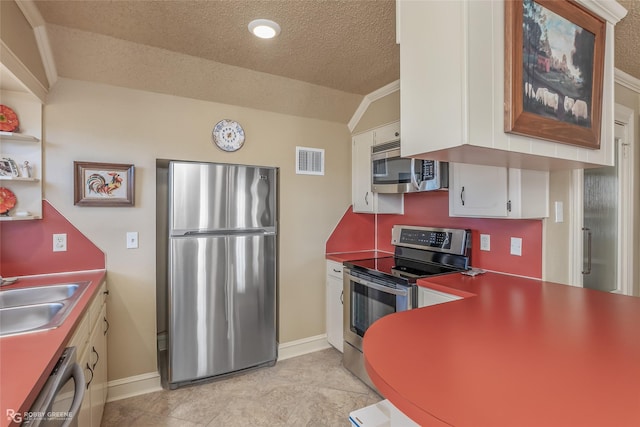 kitchen with vaulted ceiling, appliances with stainless steel finishes, sink, white cabinets, and a textured ceiling