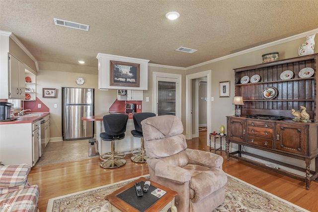 living room featuring sink, crown molding, light hardwood / wood-style flooring, and a textured ceiling