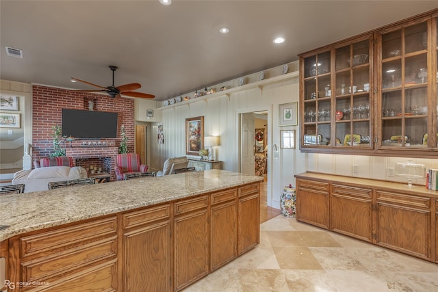 kitchen featuring a fireplace, light stone countertops, and ceiling fan