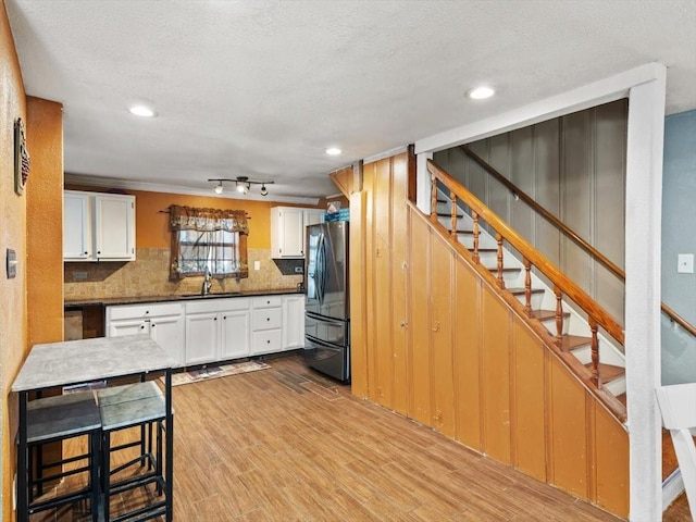 kitchen featuring white cabinetry, sink, stainless steel fridge, decorative backsplash, and light hardwood / wood-style flooring