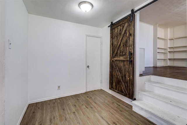 empty room with light hardwood / wood-style floors, a barn door, and a textured ceiling